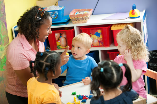 A teacher talking to four small children who are seated at a table in a classroom
